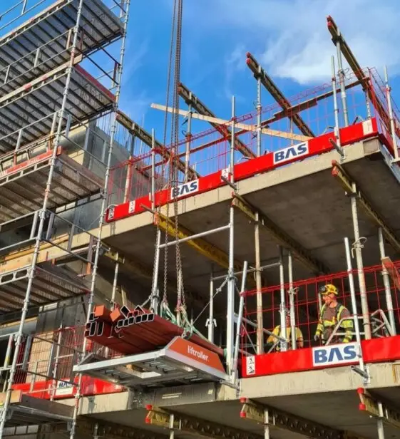 Crane lowering an orange Liftroller Floor unit onto a concrete slab edge with hi-vis crews standing by