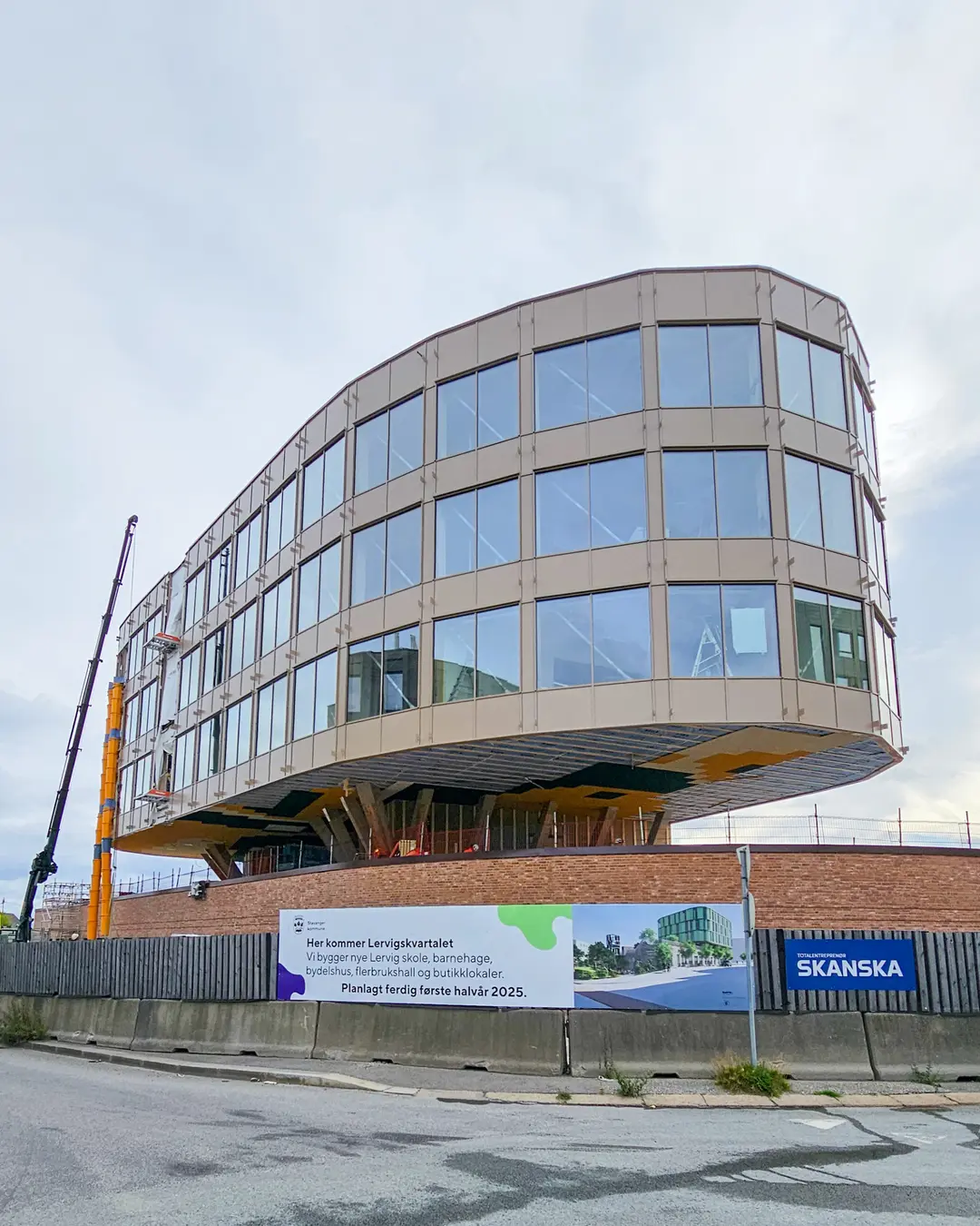 Curved glass facade of a Skanska building nearing completion with a mobile crane alongside