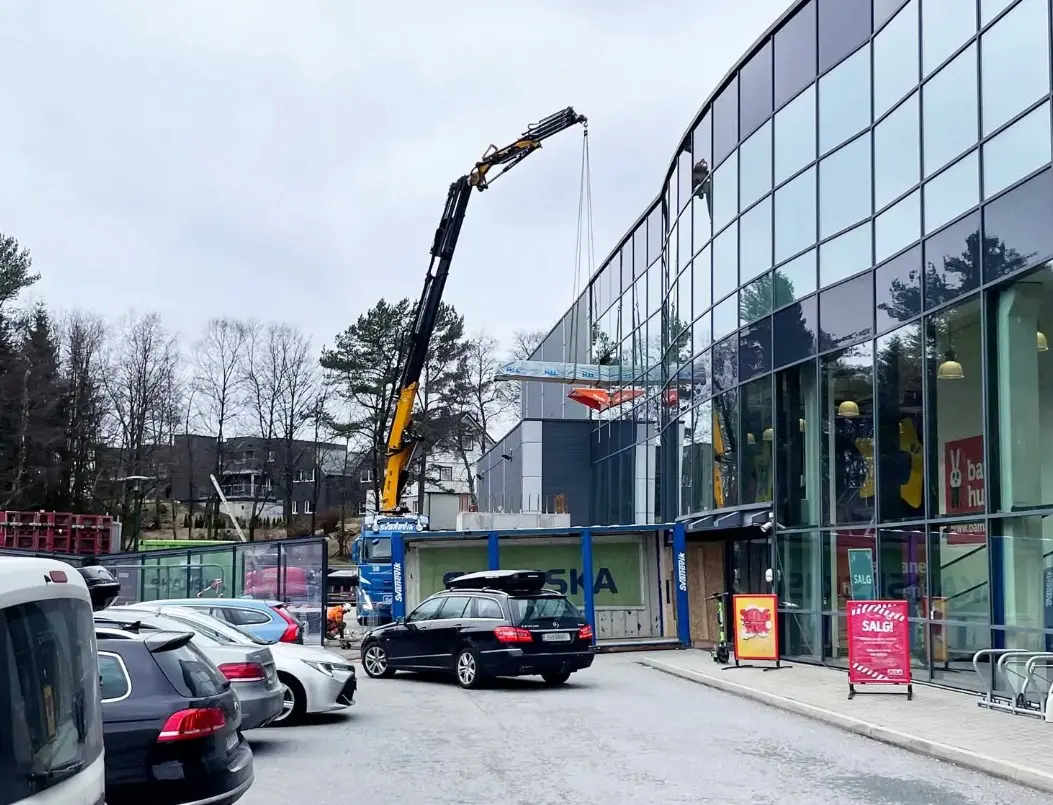 Truck mounted crane lifting a load in through the upper level of a retail building